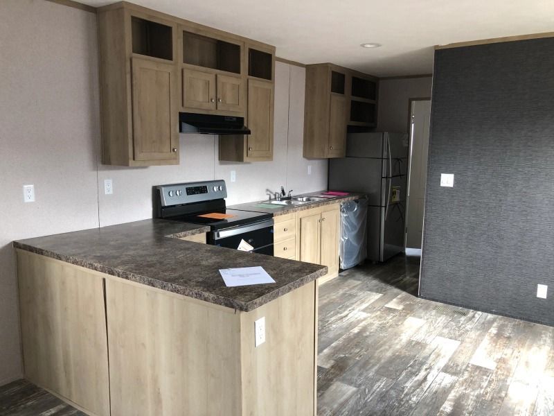 A kitchen in a mobile home with a stove , refrigerator , sink , and cabinets.