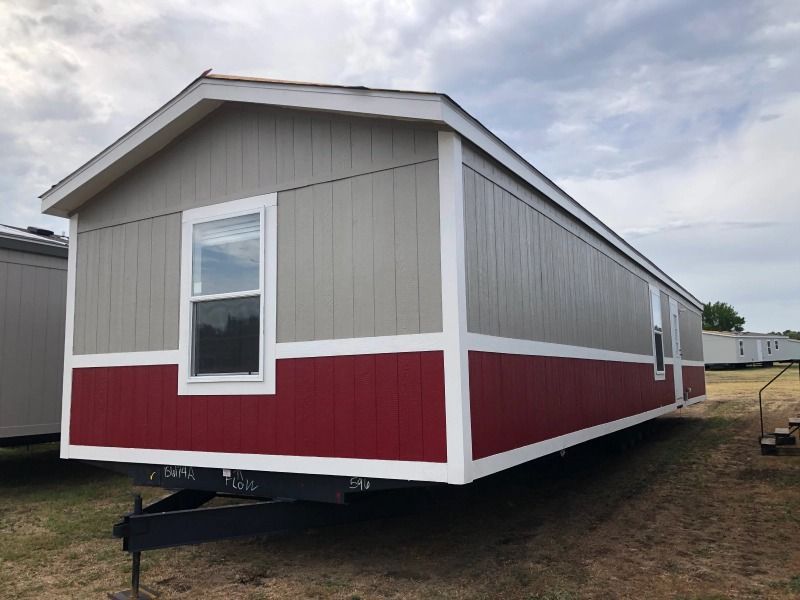 A red and gray mobile home is parked in a field.