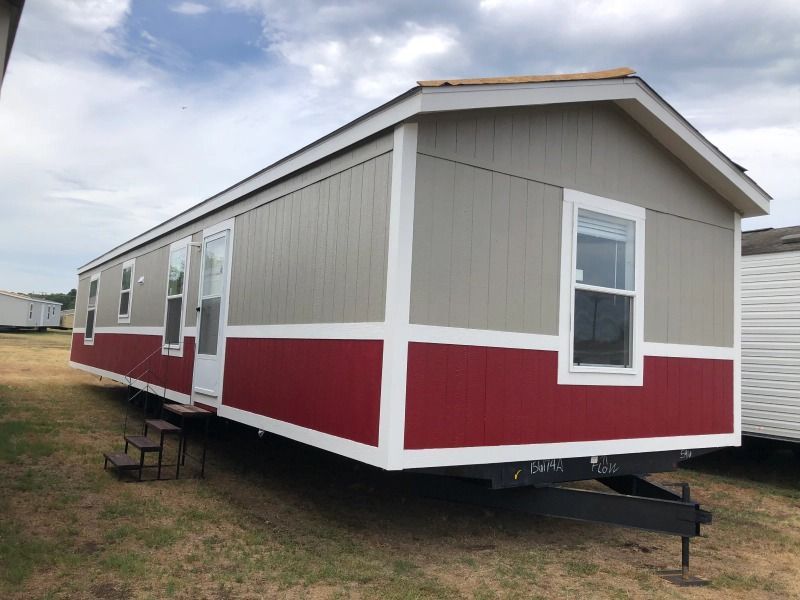 A red and white mobile home is parked in a field.