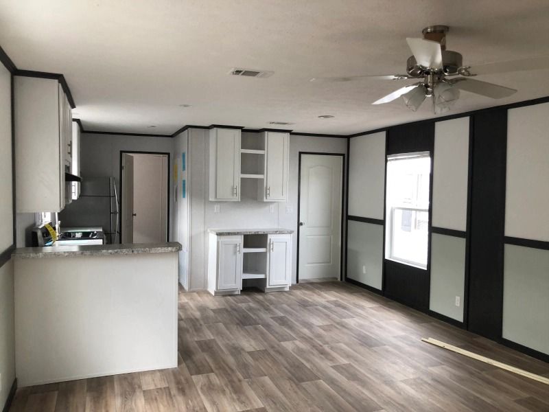 A living room with a ceiling fan and a kitchen in the background.