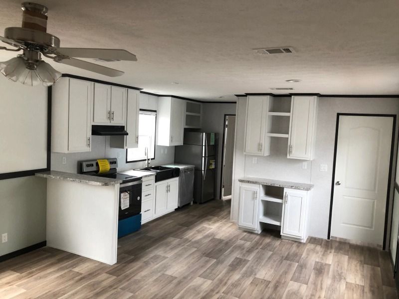 A kitchen in a mobile home with white cabinets and a ceiling fan.