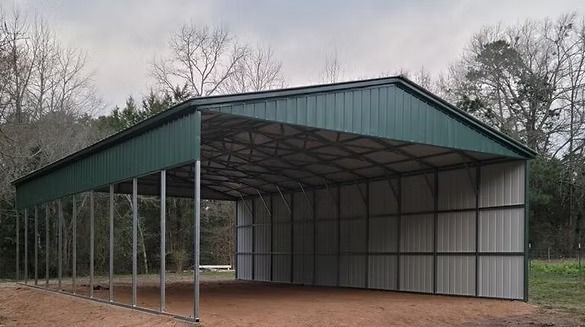 A green and white metal barn is sitting on top of a dirt field.