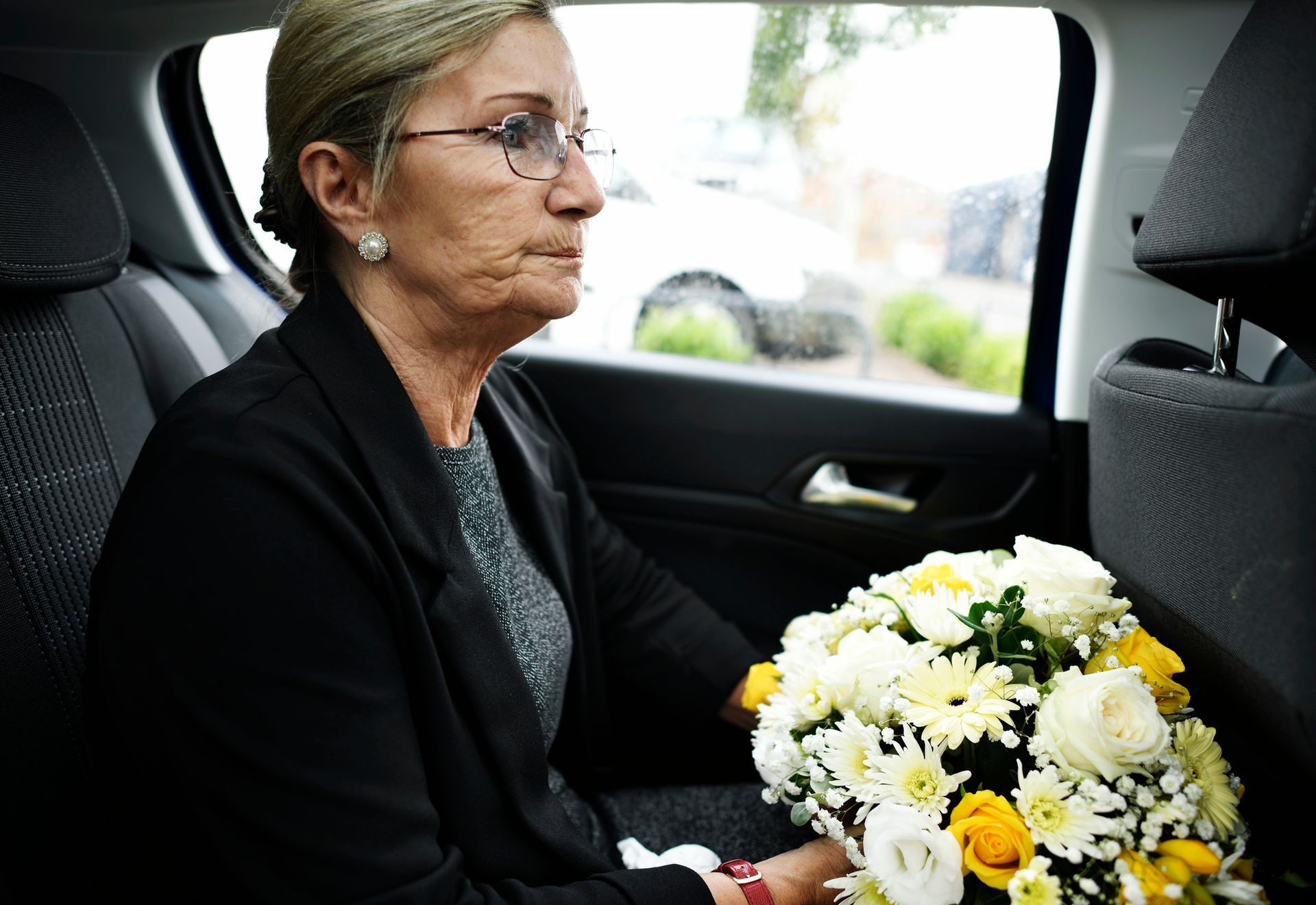 A woman is sitting in the back seat of a car holding a bouquet of flowers.