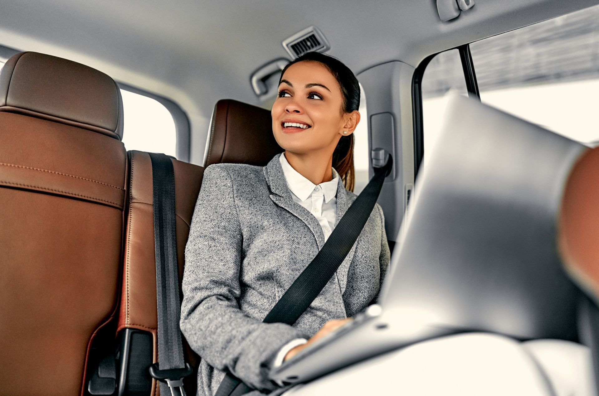 A woman is sitting in the back seat of a car with a laptop.