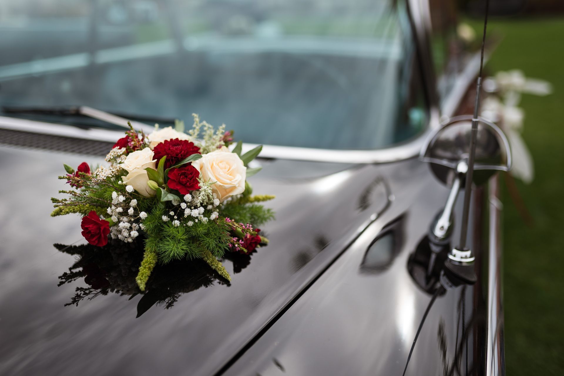 A bouquet of flowers is sitting on the hood of a black car.