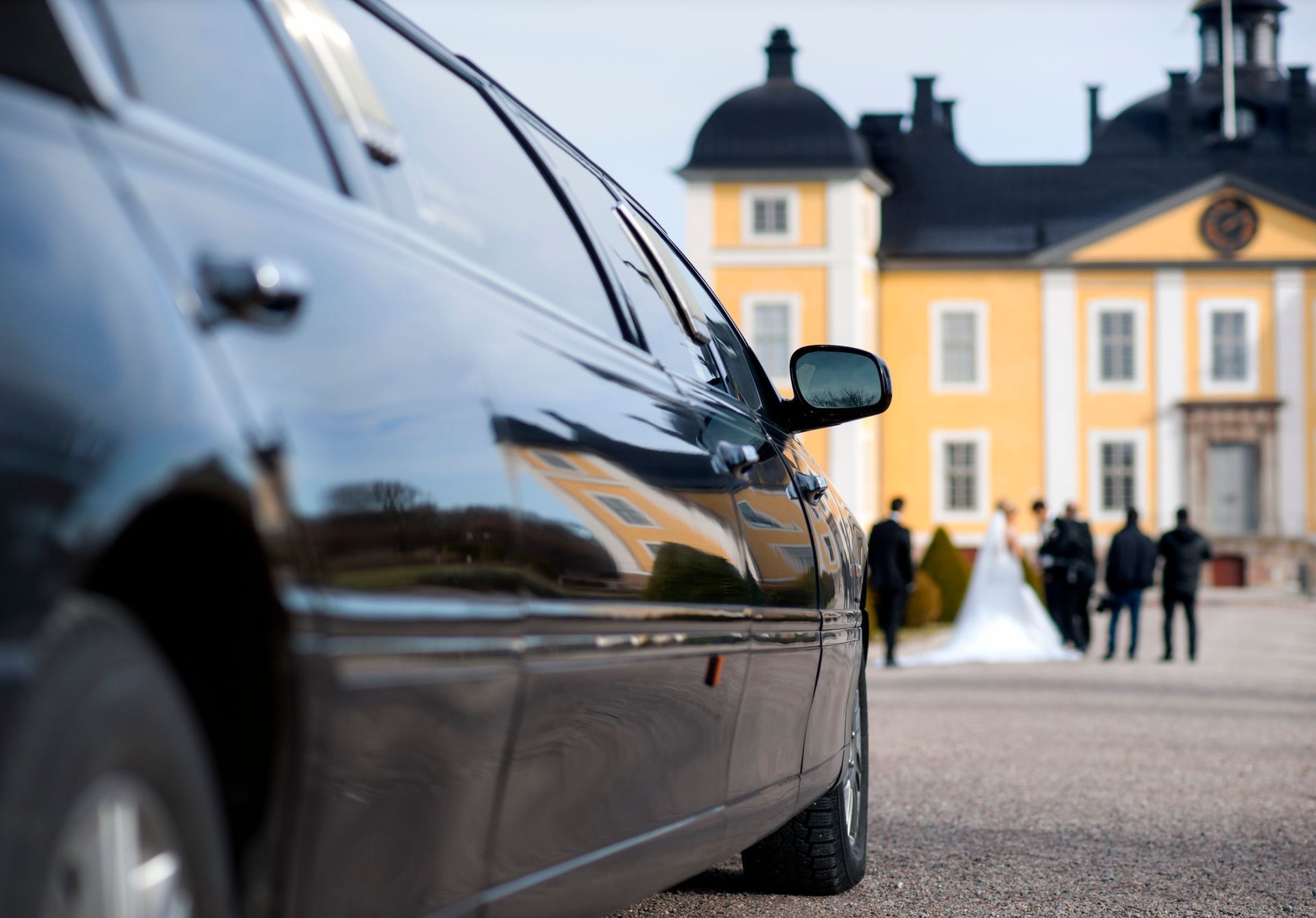A black limousine is parked in front of a yellow building.