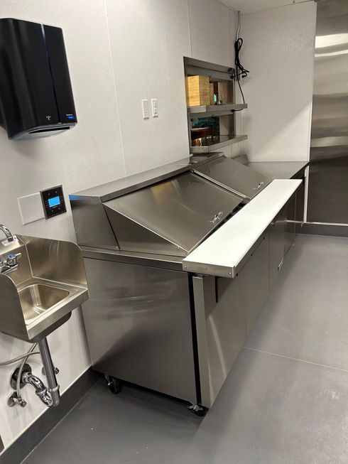 Stainless steel commercial kitchen prep station with sink and shelving.