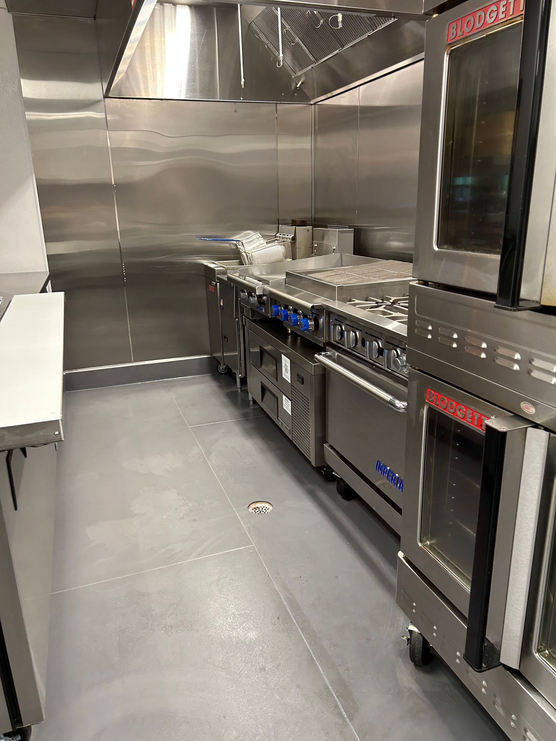 Commercial kitchen with stainless steel appliances: ovens, stove, and ventilation hood.