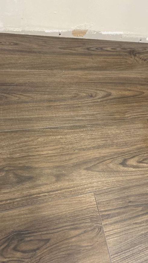 Dark wood-look flooring meets a light-colored wall. Small discoloration at the wall's base.