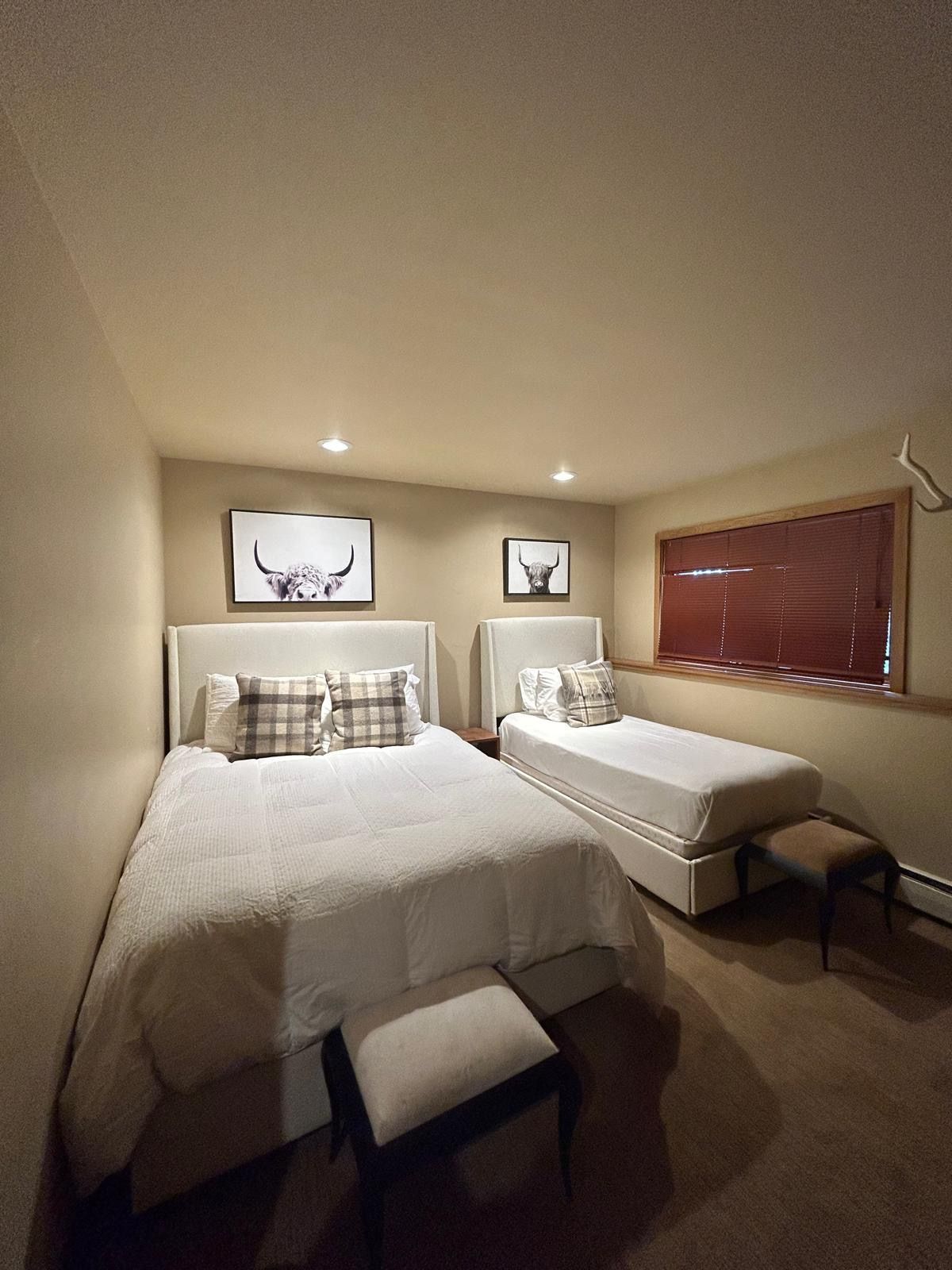 Two twin beds in a room with matching decor. Artwork on the walls, with a small stool at the foot of each bed.