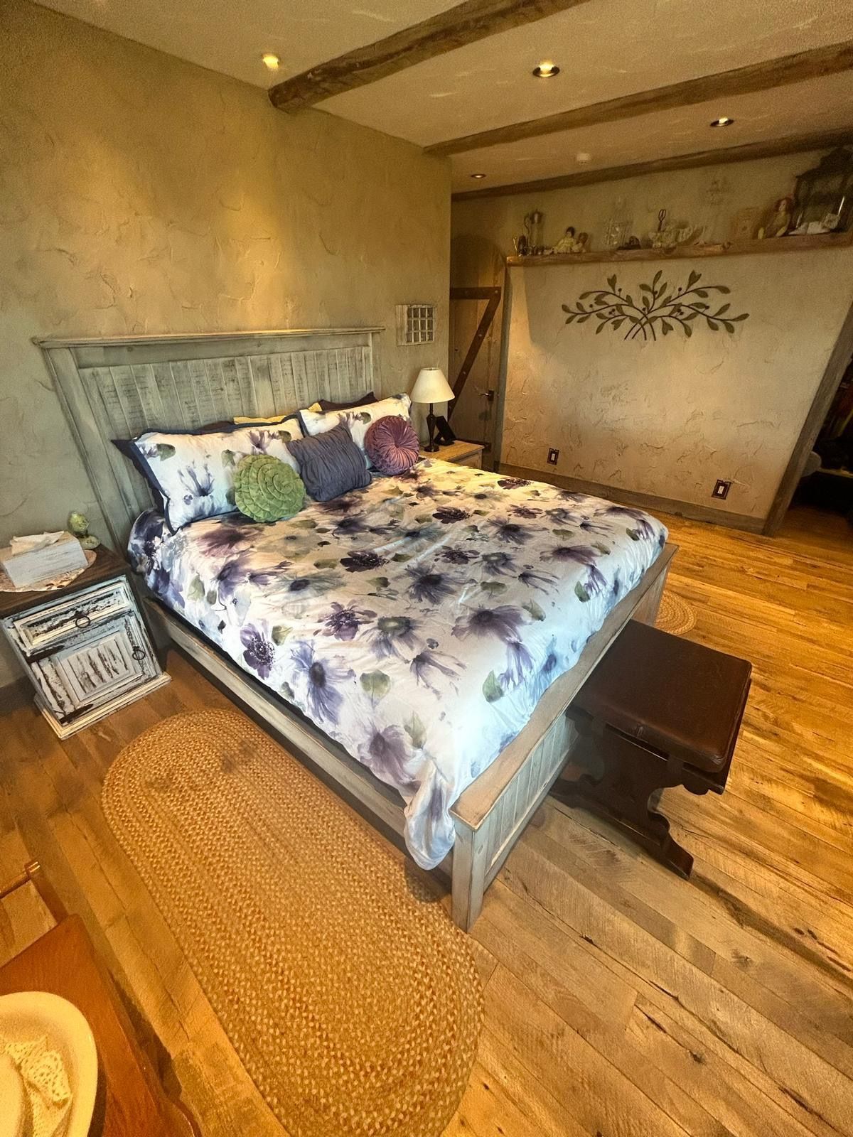 Bedroom with wood floors, bed with purple floral bedding, and decorative wall art.