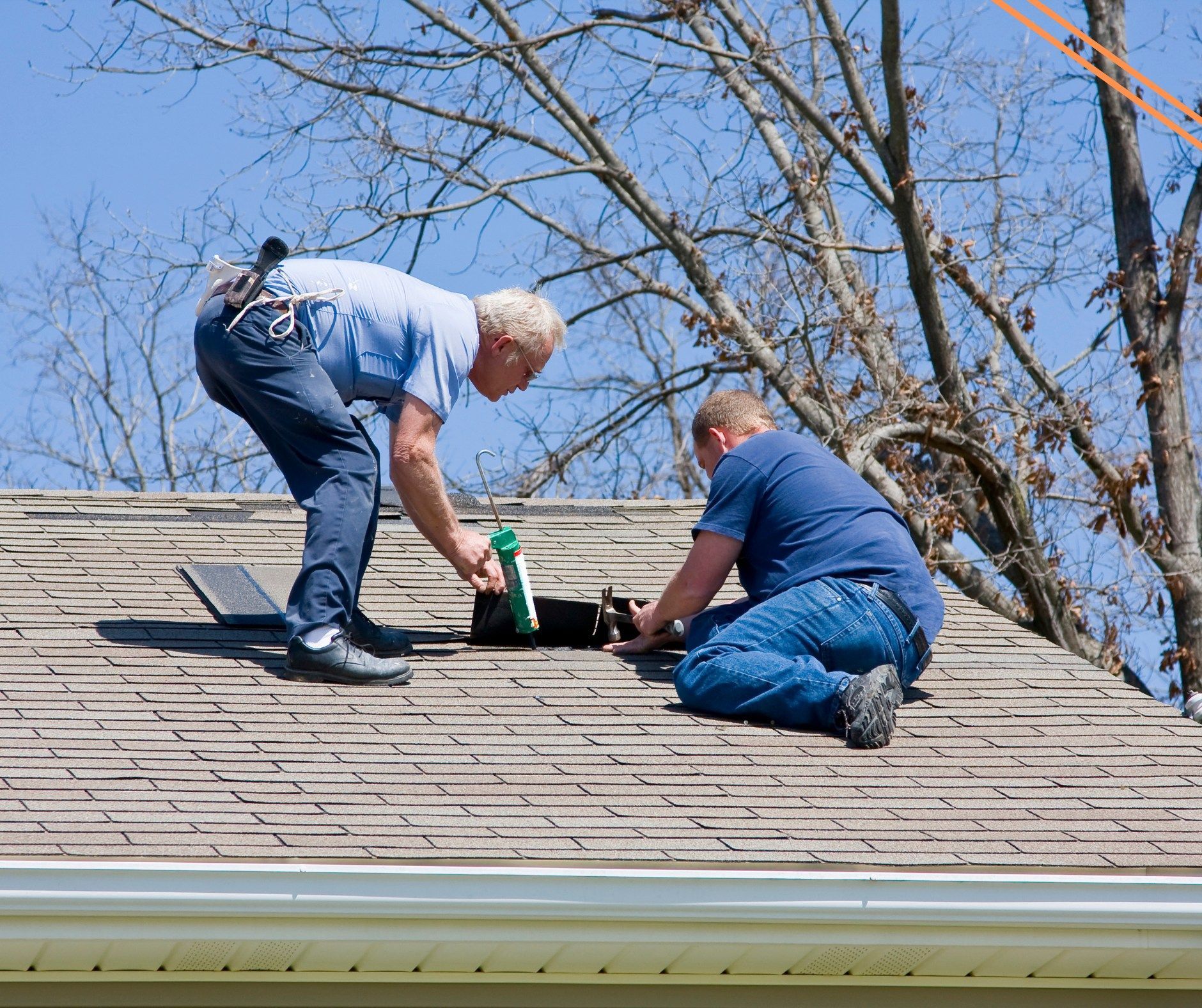 Two men repairing a roof, one using a tool, the other kneeling near an opening. Sunlight bathes the scene, and the sky is blue.