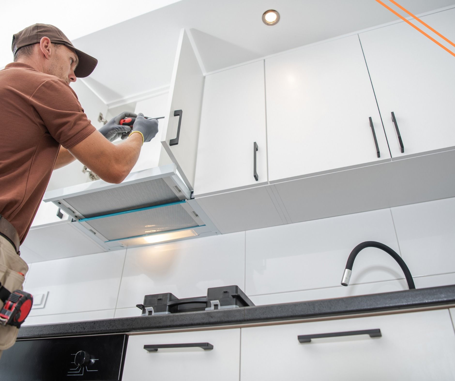 A man installing a range hood in a modern white kitchen, using a power drill.