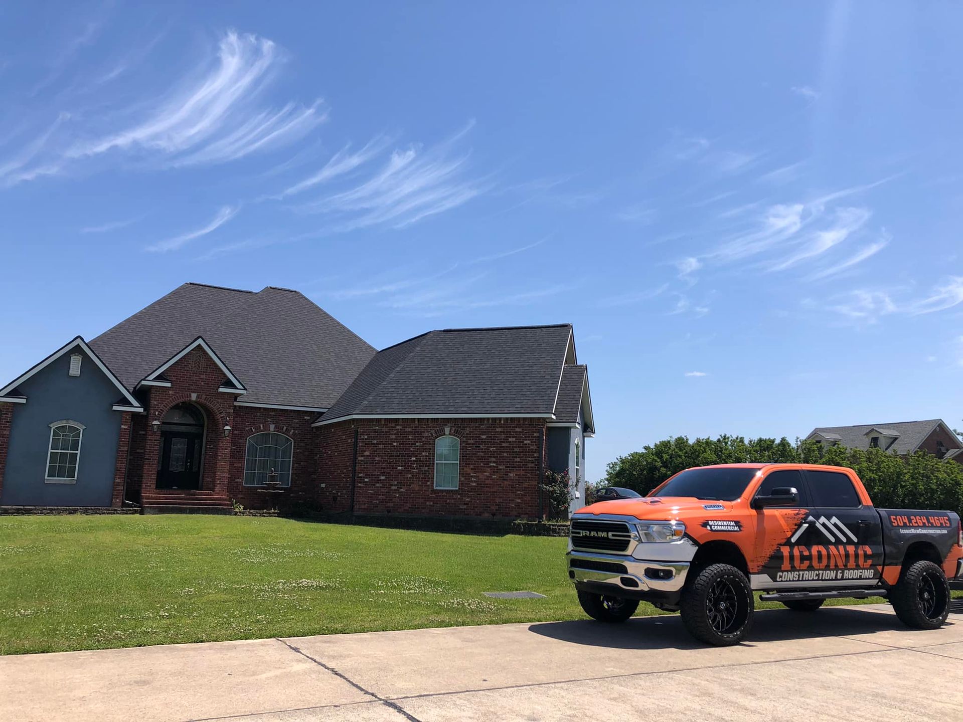 An orange truck with logo parked in front of a brick house with a dark roof on a sunny day.