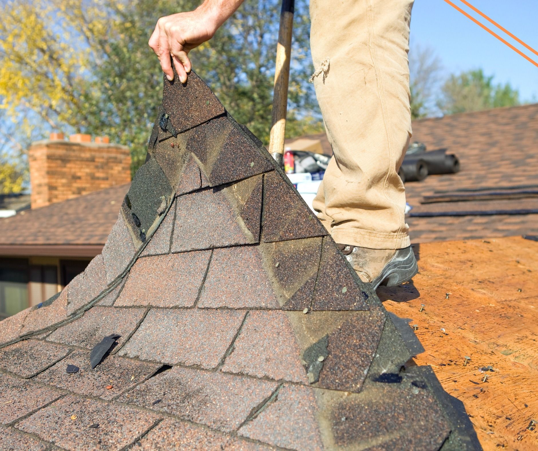 A person removing old asphalt roof shingles from a rooftop, showing weathered brown shingles and a sunny outdoor setting.