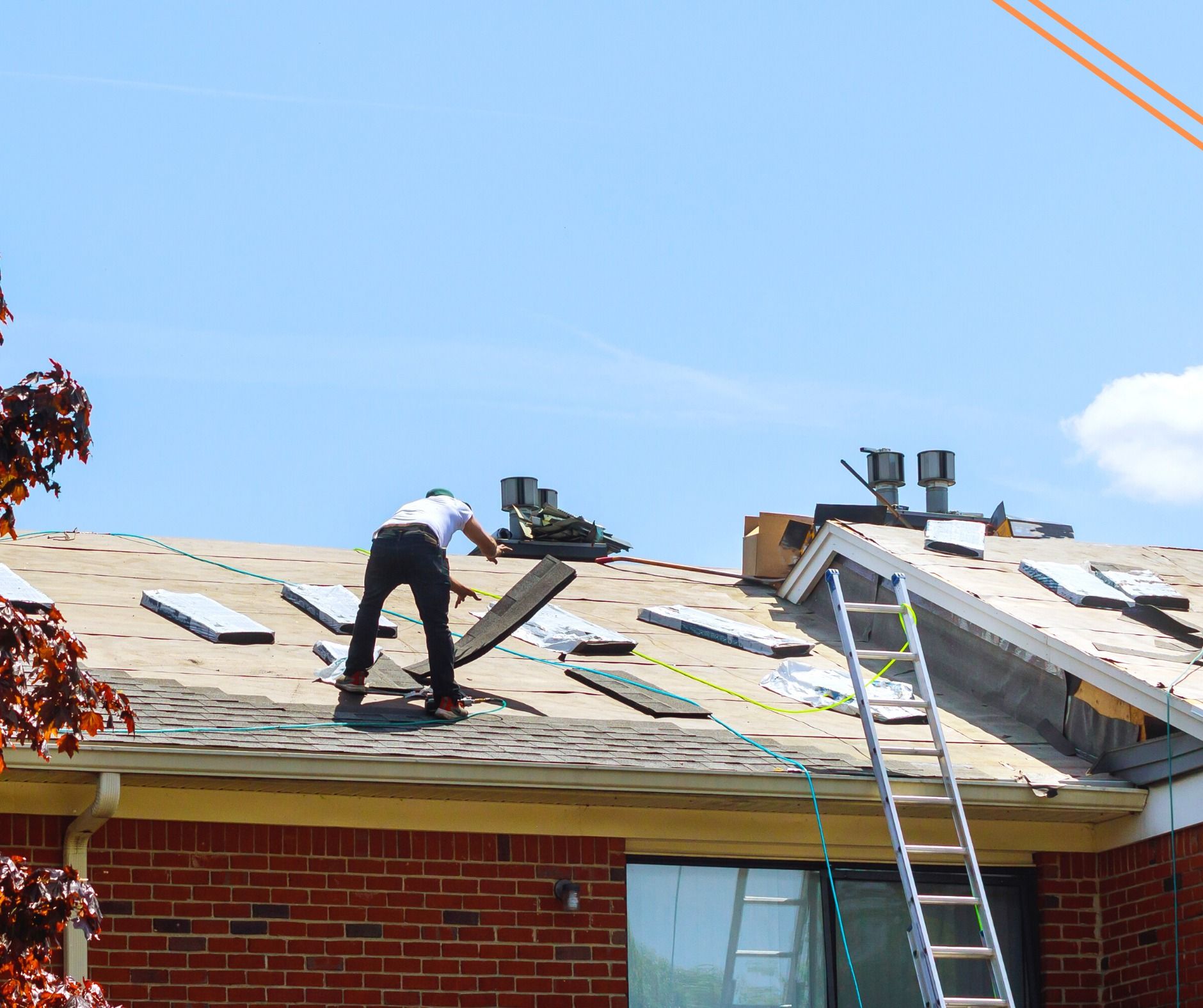 Roofer on a rooftop removing old shingles, ladder propped up next to a chimney, clear blue sky in the background.