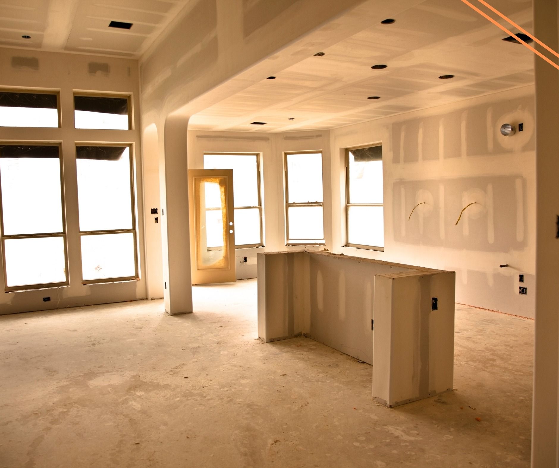 Interior of a room under construction, with exposed drywall, a partial kitchen island, and windows.