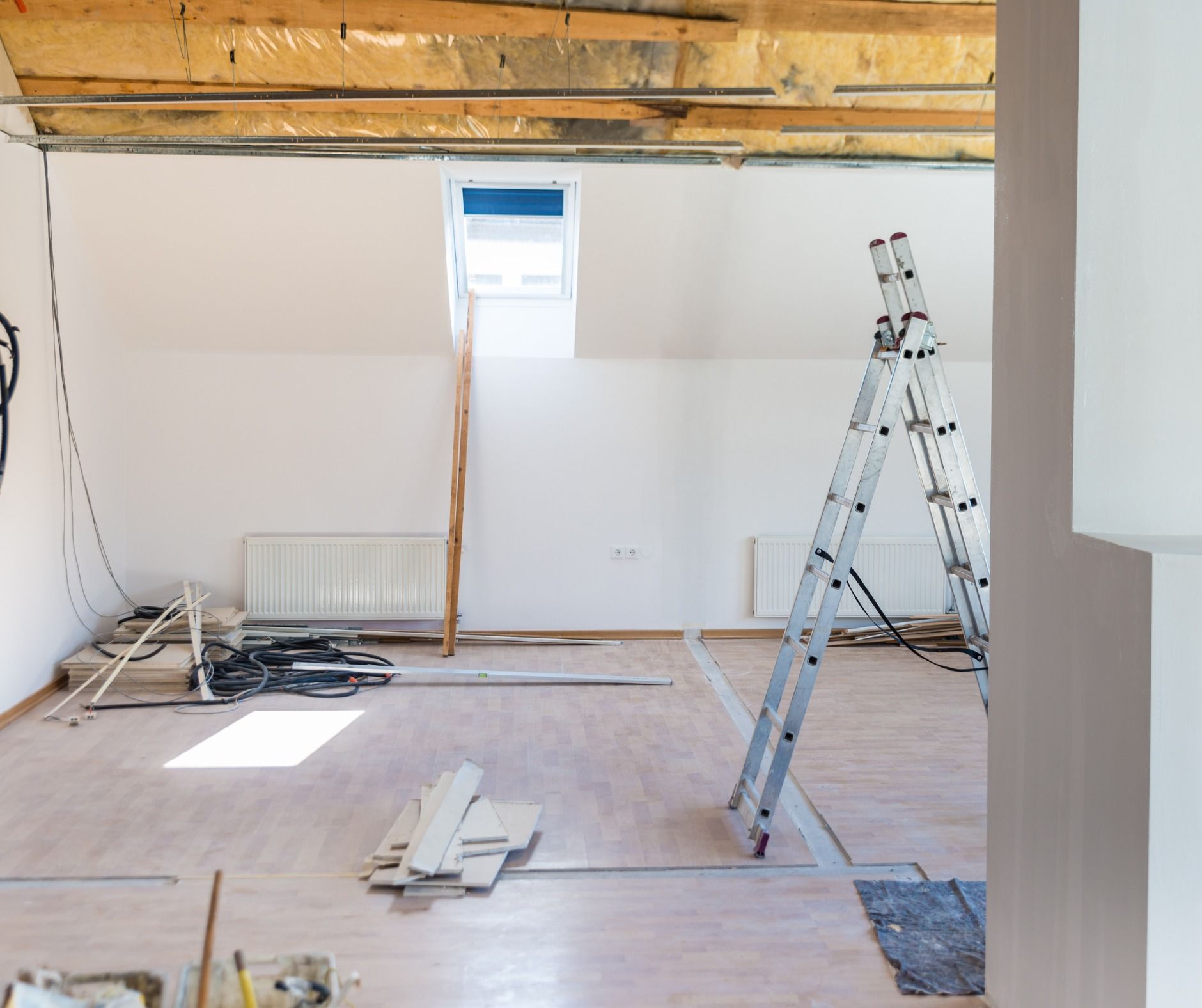 Interior of a room under renovation with exposed wooden beams, white walls, a skylight, and a ladder.