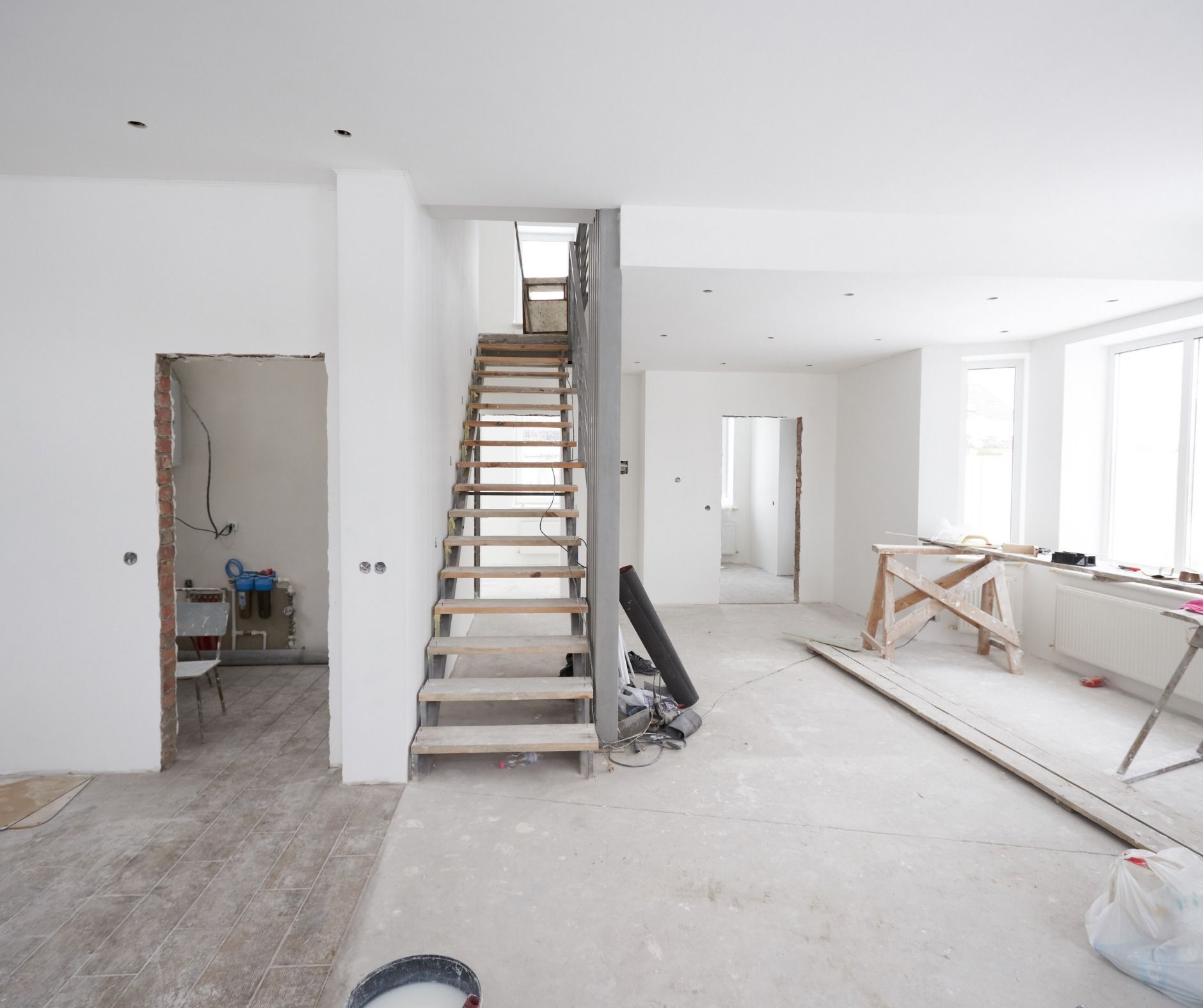 Interior renovation, showing a staircase, open doorways, and unfinished walls. Construction materials and tools are visible throughout the room.