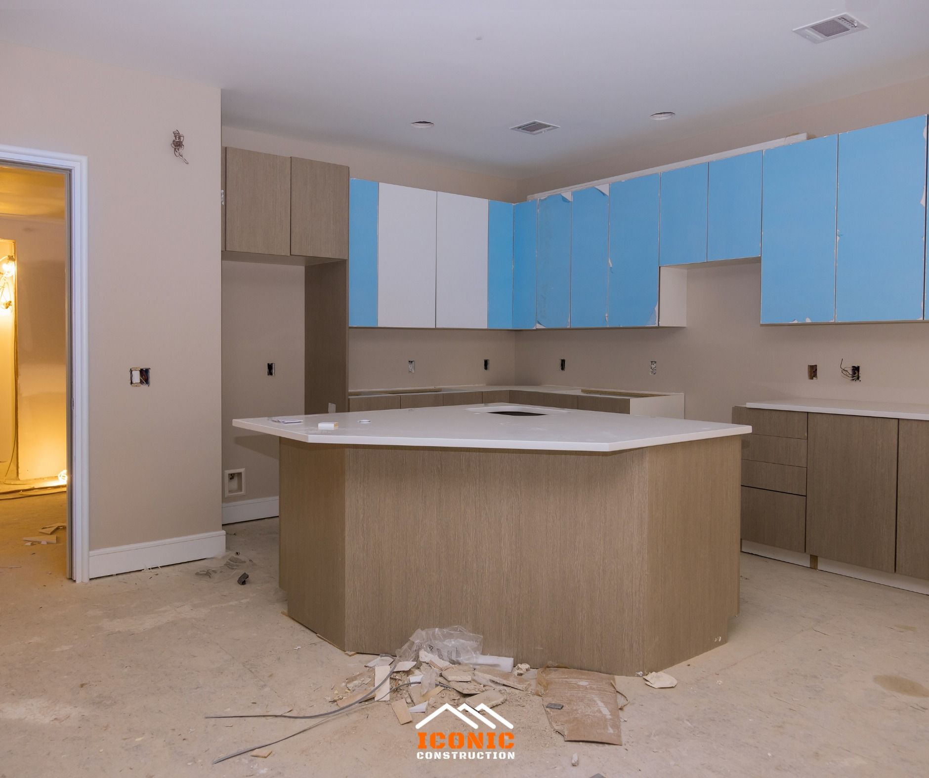 Kitchen undergoing renovation with light blue and beige cabinets, an island, and light-colored walls.