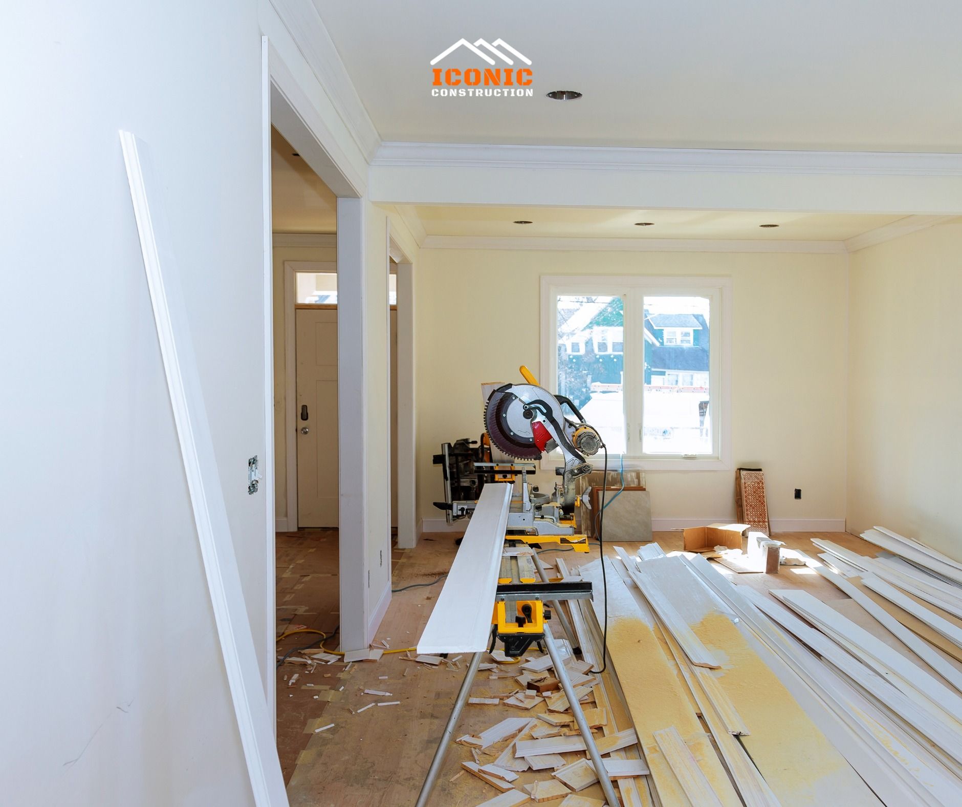 Interior of a house under renovation, with a saw, wood planks, and a door. Walls are white.