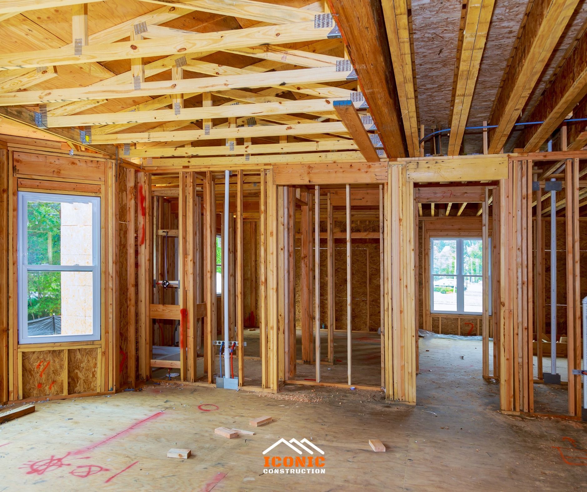 Interior view of a house under construction, showing wooden framing, walls, and windows.