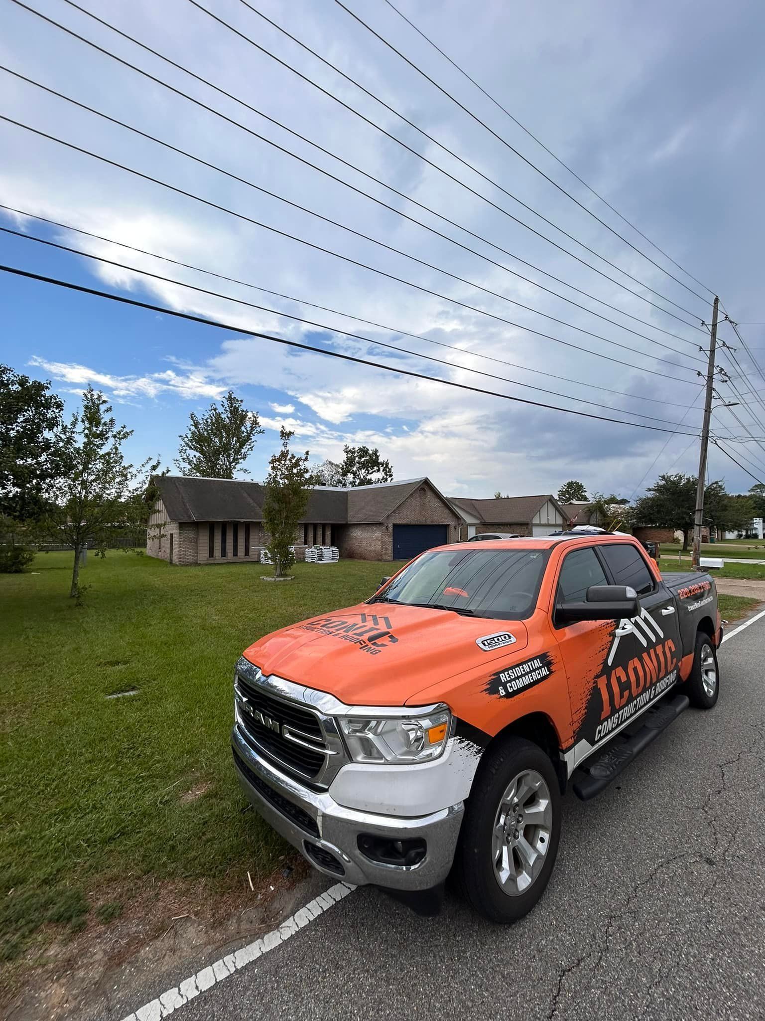 Orange and black wrap on a truck parked by a road, with houses in the background. Overcast sky and power lines overhead.