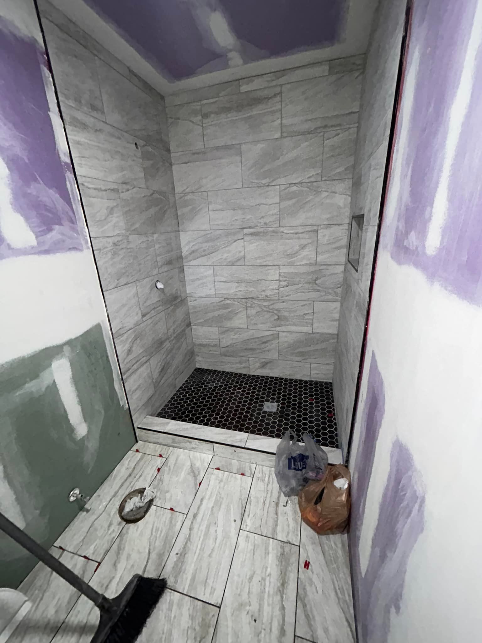 A bathroom under construction with tiled shower and floor, partially sheet-rocked walls, and construction debris.
