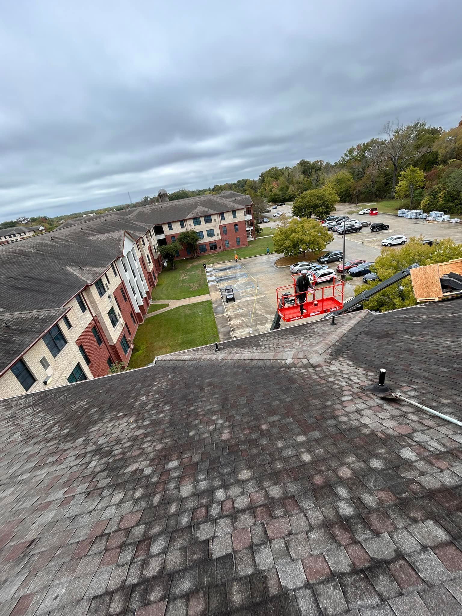 View of a multi-story apartment building with workers on a roof; cloudy sky overhead.