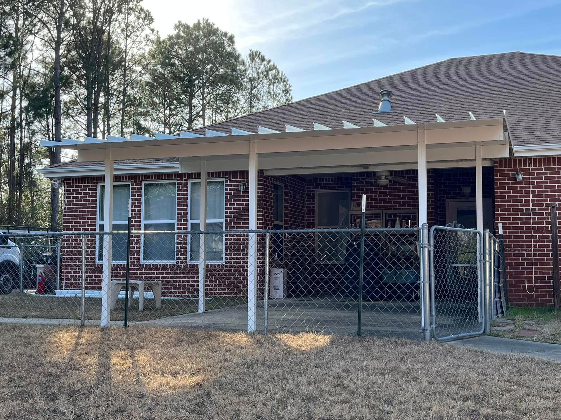 A brick home with a covered porch, enclosed by a chain-link fence. The yard has dry grass.