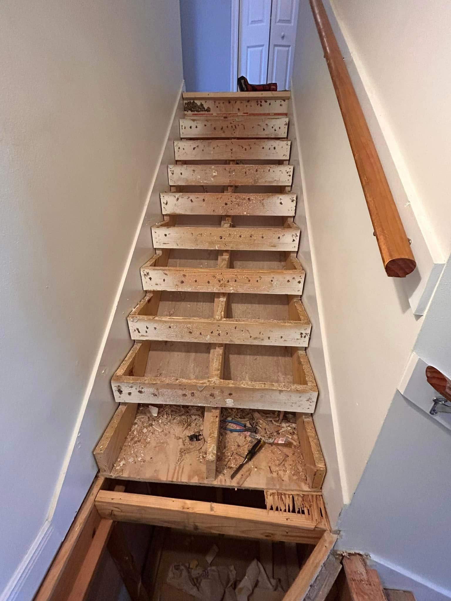Staircase undergoing renovation. Damaged wooden steps are exposed; the walls are painted beige.
