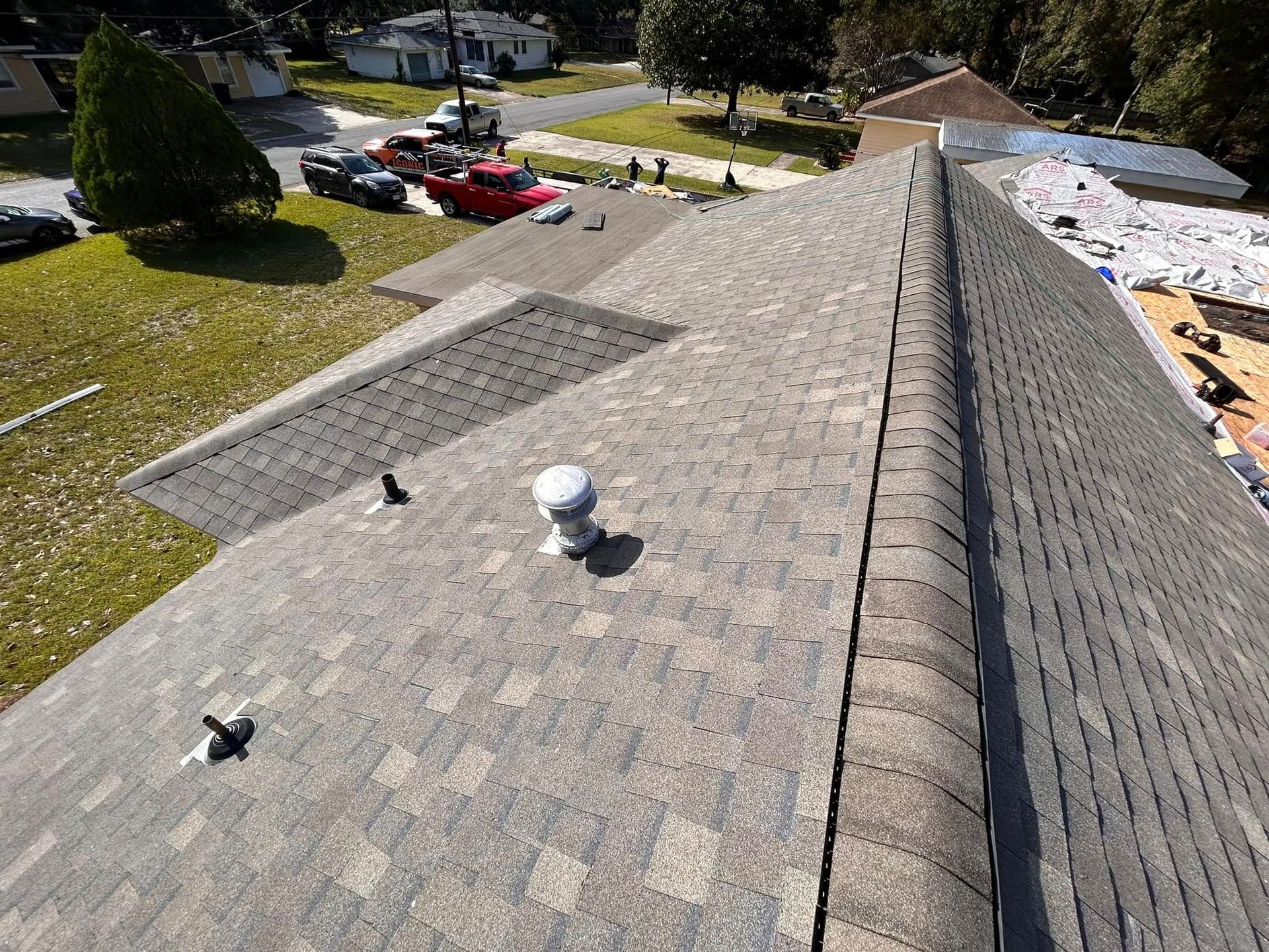 Overhead view of a roof with gray shingles, a vent, and a partially visible roof replacement in progress.