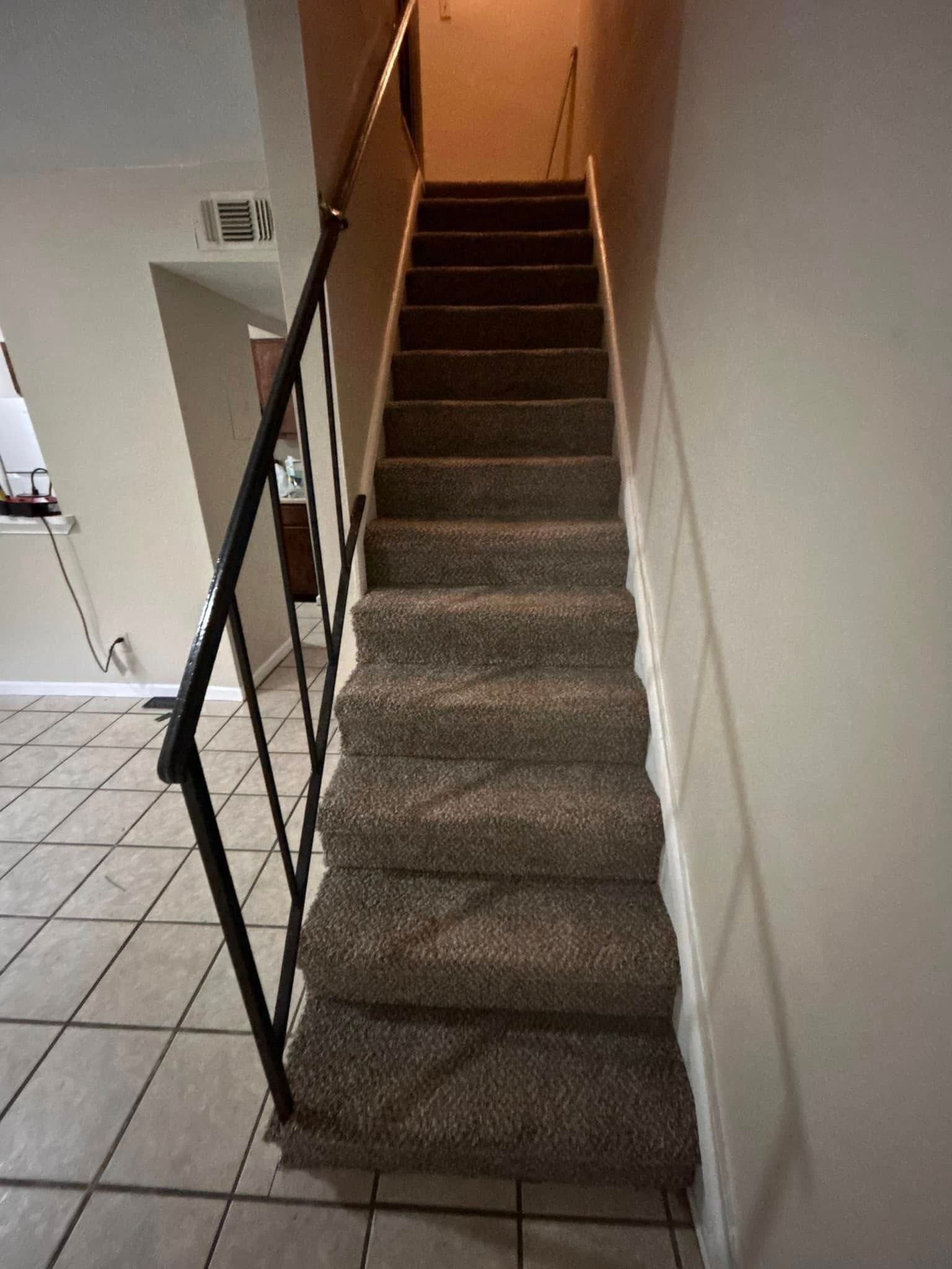 Staircase with brown carpet and black metal railing leading upwards, located between beige walls.