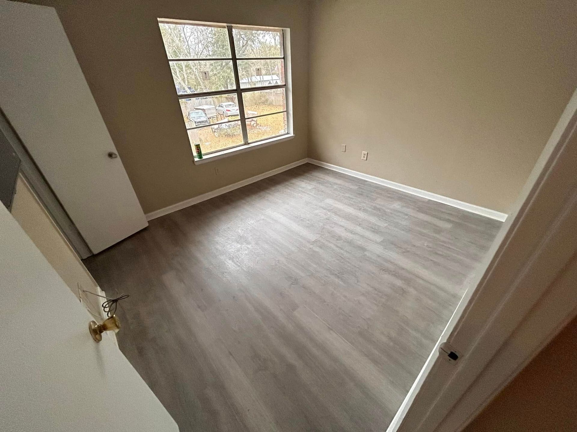 Empty bedroom with gray flooring, tan walls, a window, and a closed white door.
