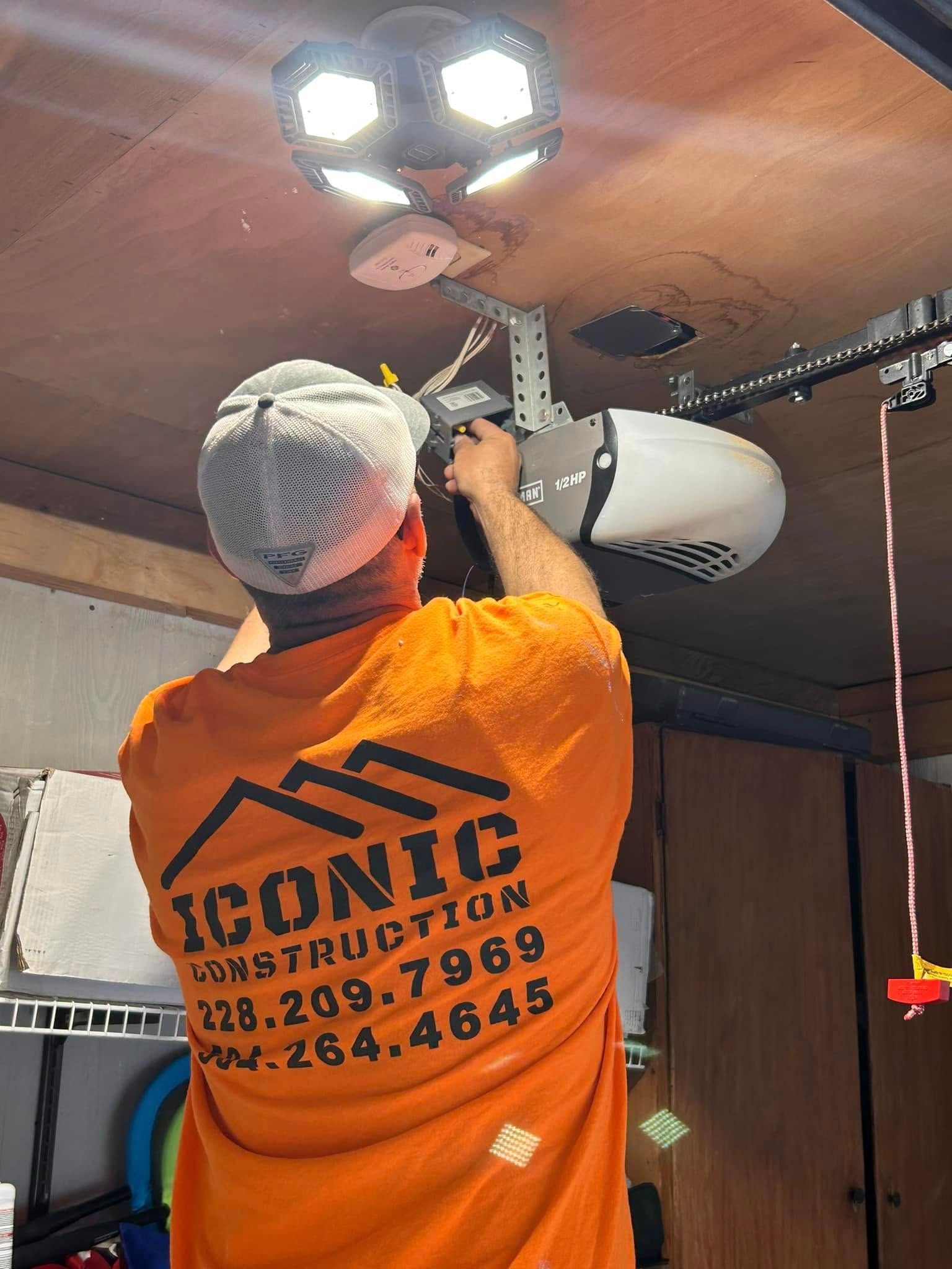 A man in an orange shirt installs a garage door opener in a garage. He is reaching up to work on the opener.