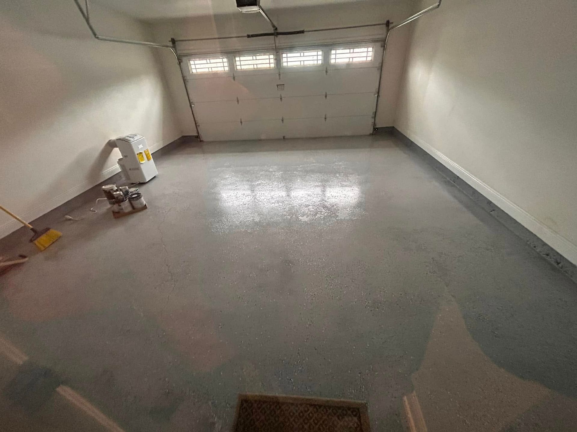 An empty garage with a newly coated gray floor. A closed white garage door is in the background.