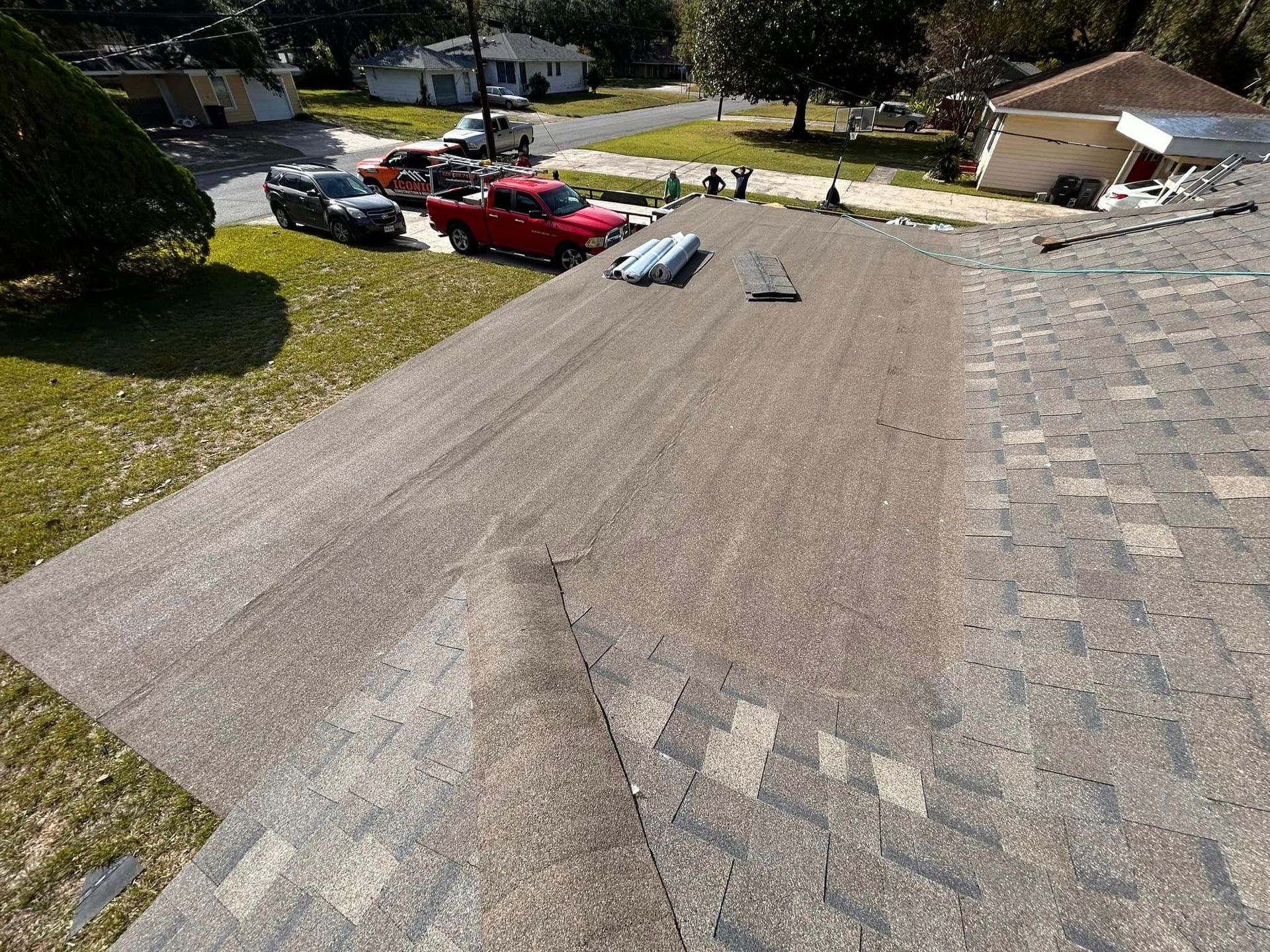 Roof being worked on with a truck parked on the street. Workers stand nearby with supplies.