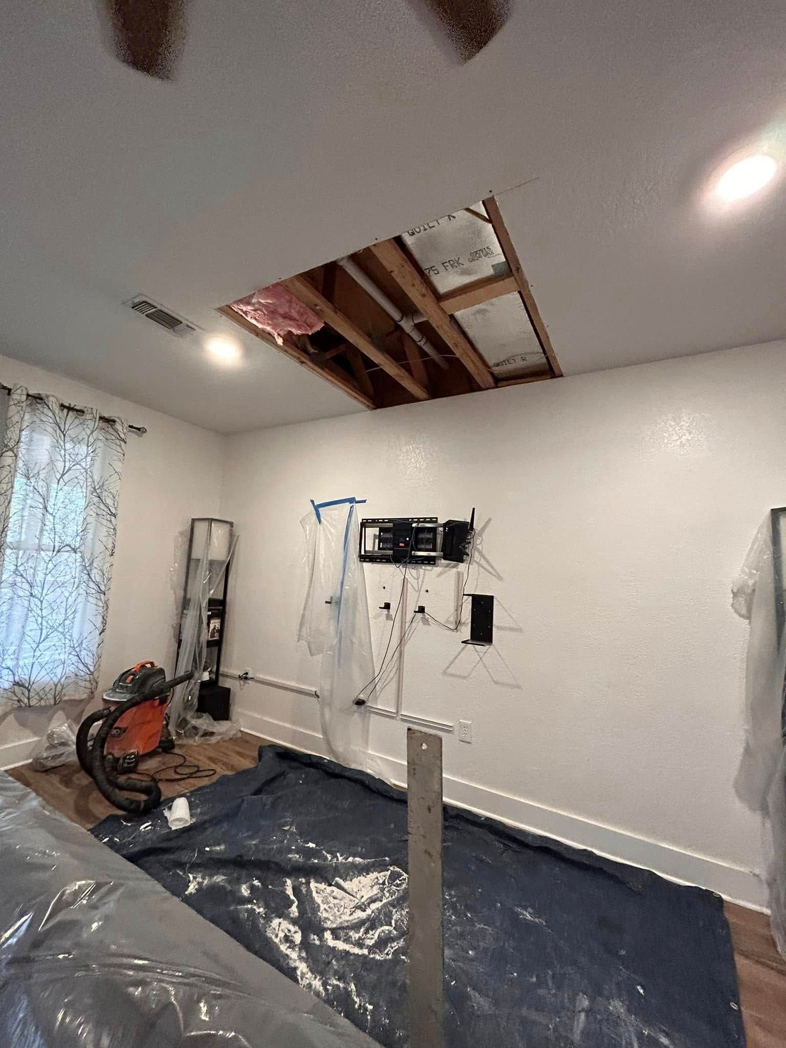 Room with a large hole in the ceiling, likely under renovation. Tools and a protective tarp are visible.