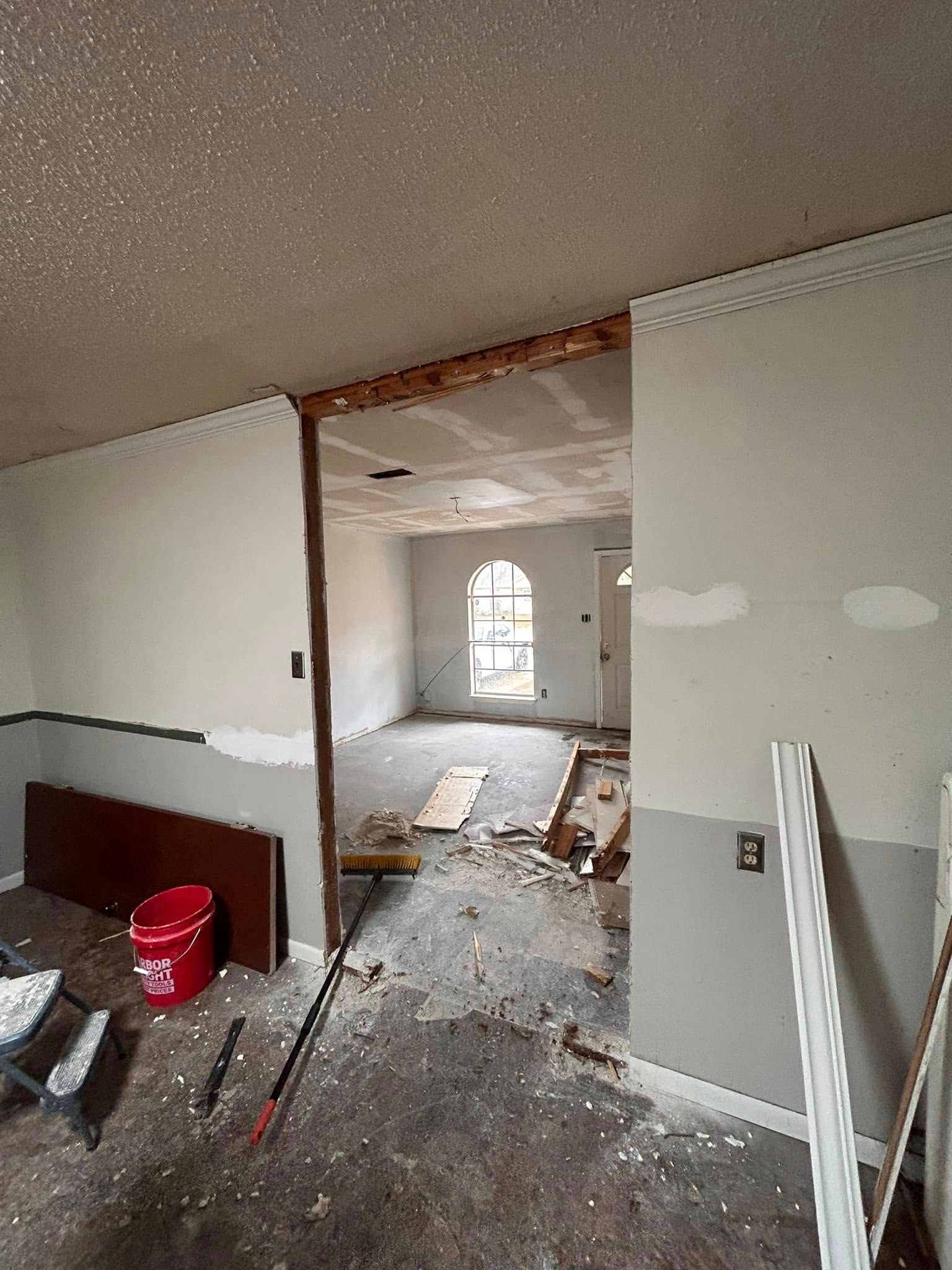 Interior view of a home under construction. A doorway is framed by partially finished walls, debris litters the floor.