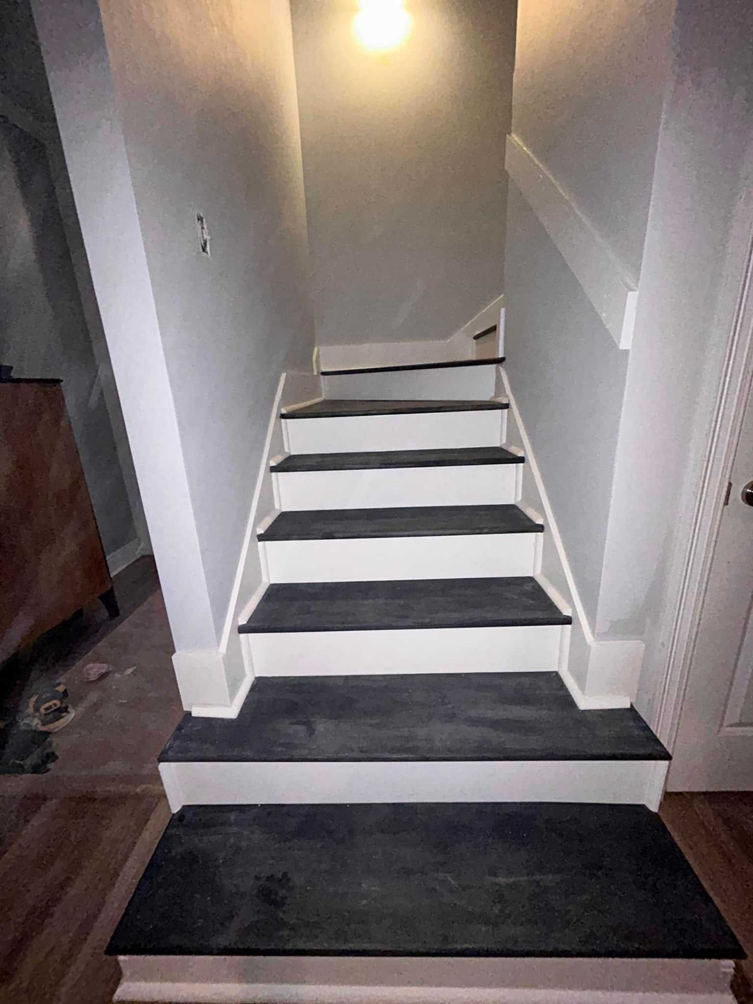 Staircase painted white and black, leading upward. Walls are light gray; overhead light.