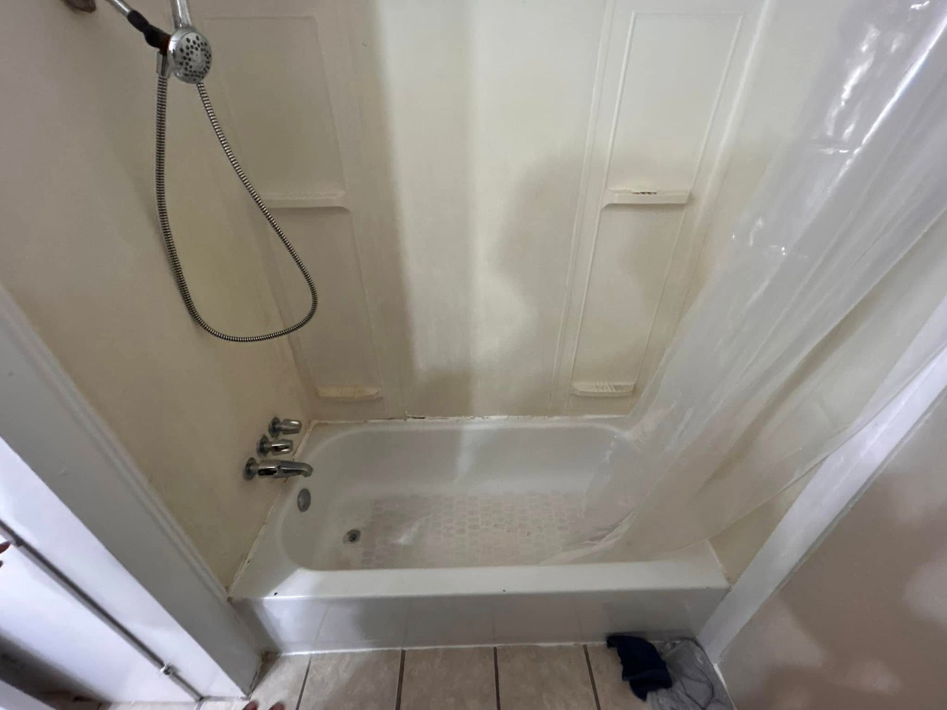 An empty white shower stall with a tub, shower head, and clear shower curtain. Three small shelves are on the back wall.