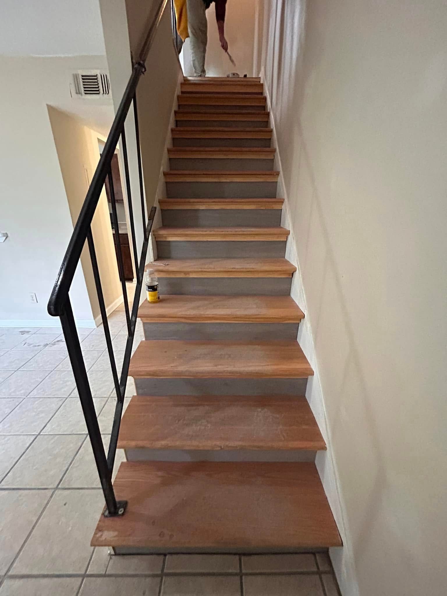 Staircase with wooden steps and a black iron railing. A person is working on the stairs near the top.