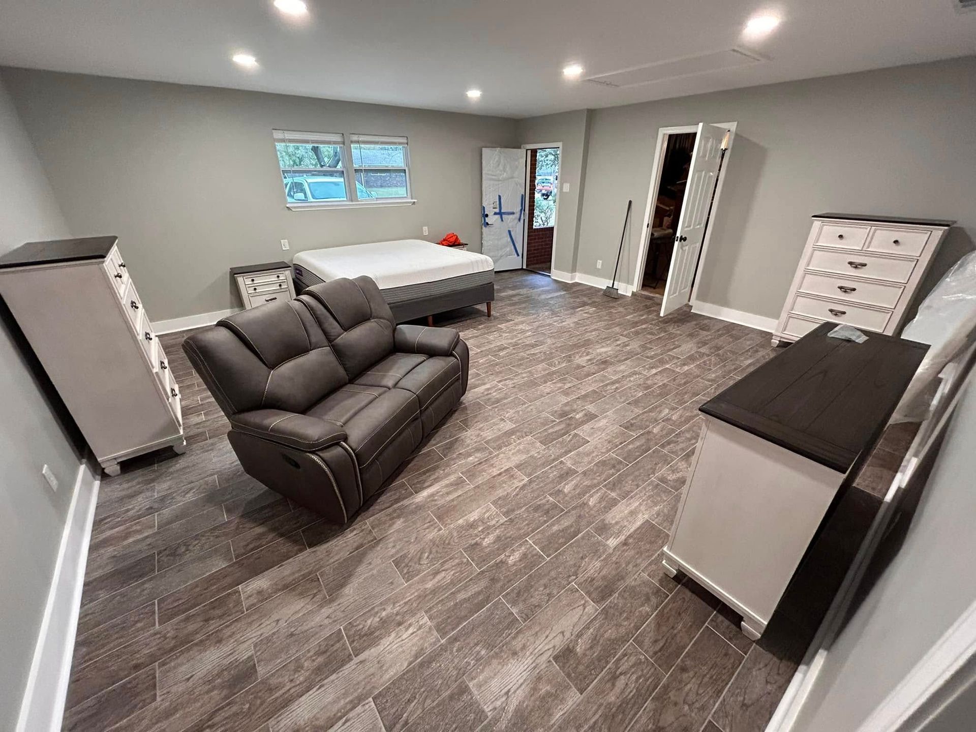 A room with furniture, including a sofa, bed, and dressers, with gray walls and tile flooring.