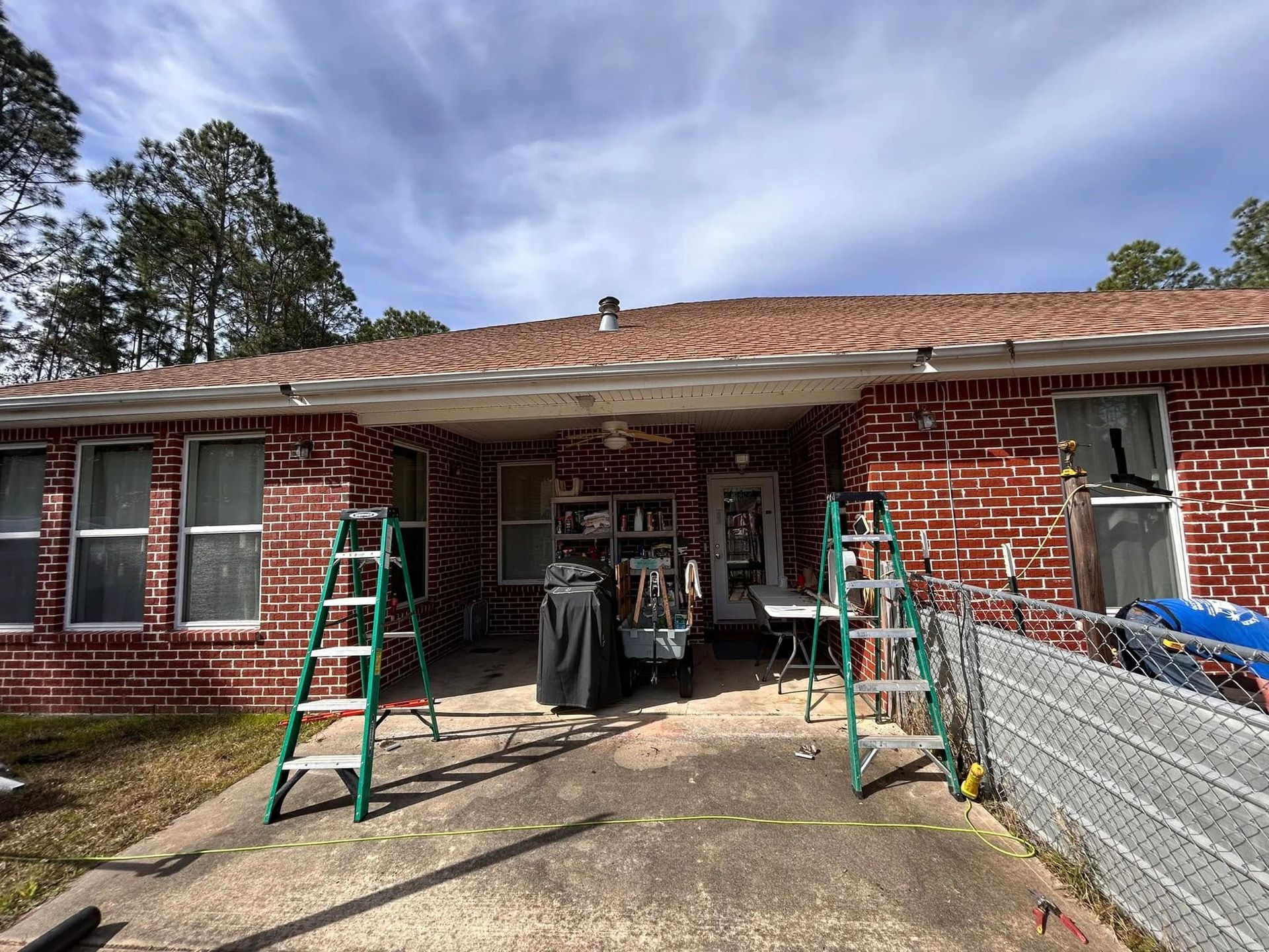 Red brick house exterior with a concrete patio. Two green ladders stand in front of the porch where items are stored.
