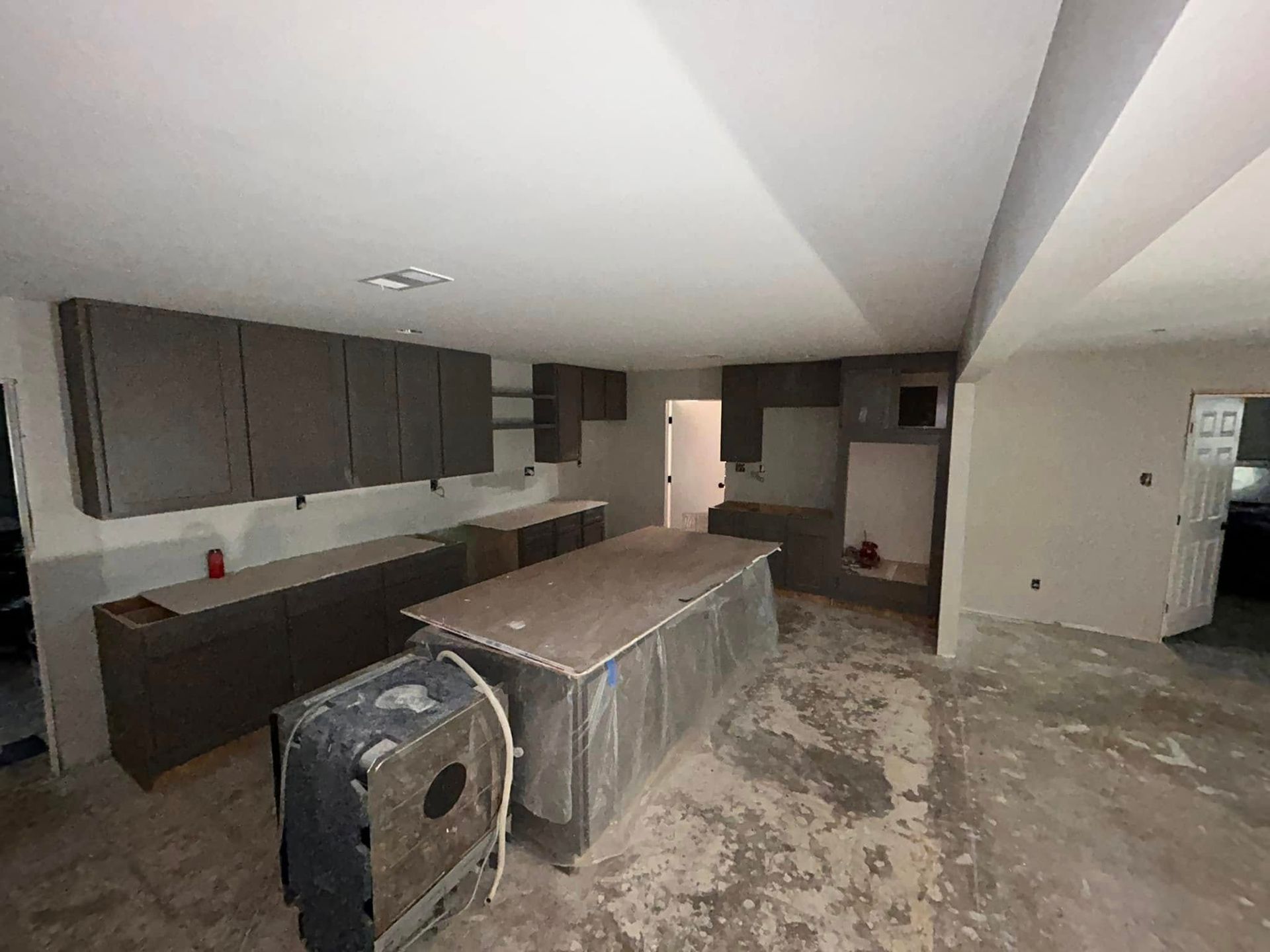 A kitchen under renovation with gray cabinets, an island, and exposed concrete flooring.