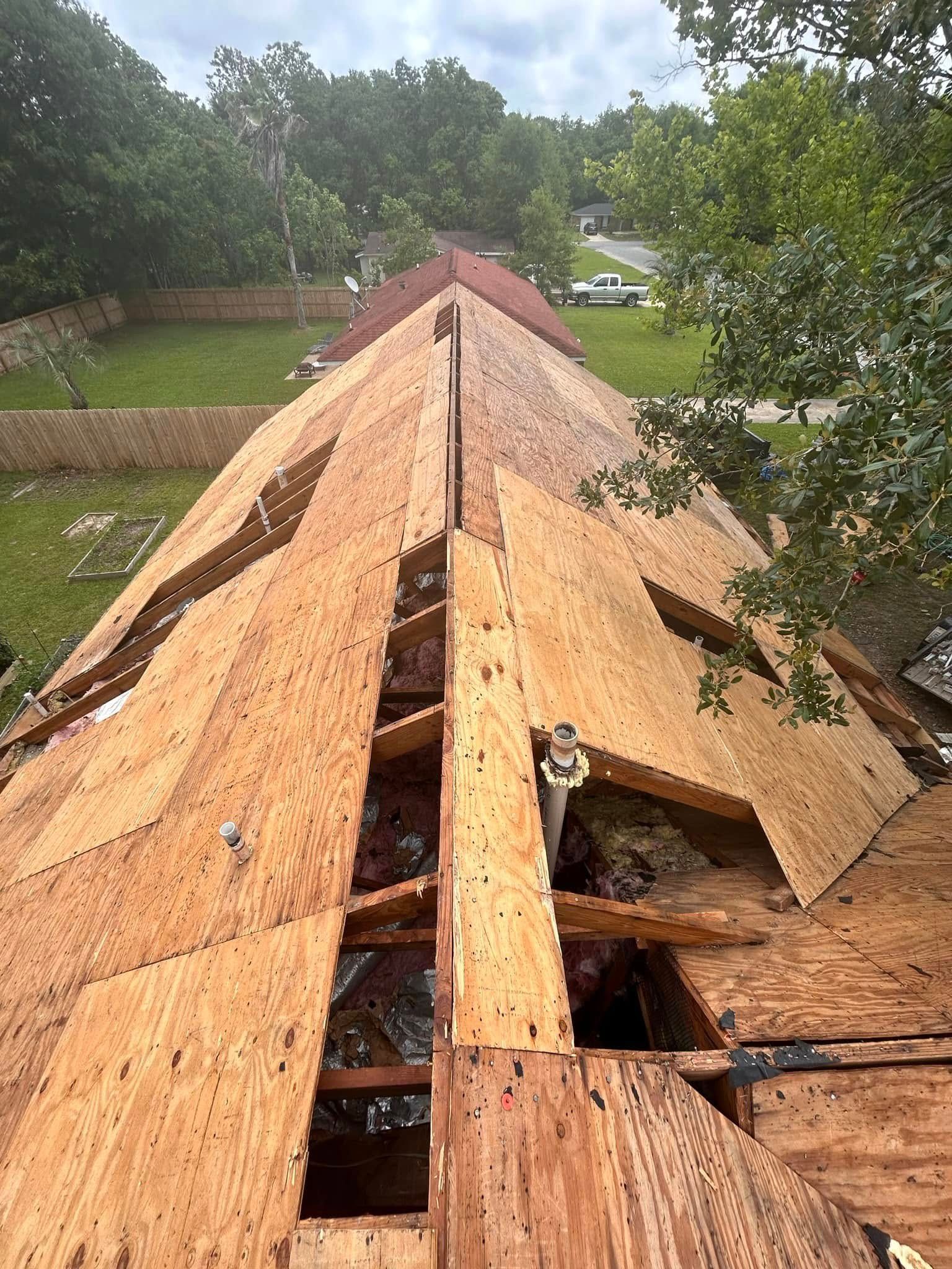 A rooftop with exposed wooden planks. Construction is in progress with a view of the surrounding green landscape and trees.