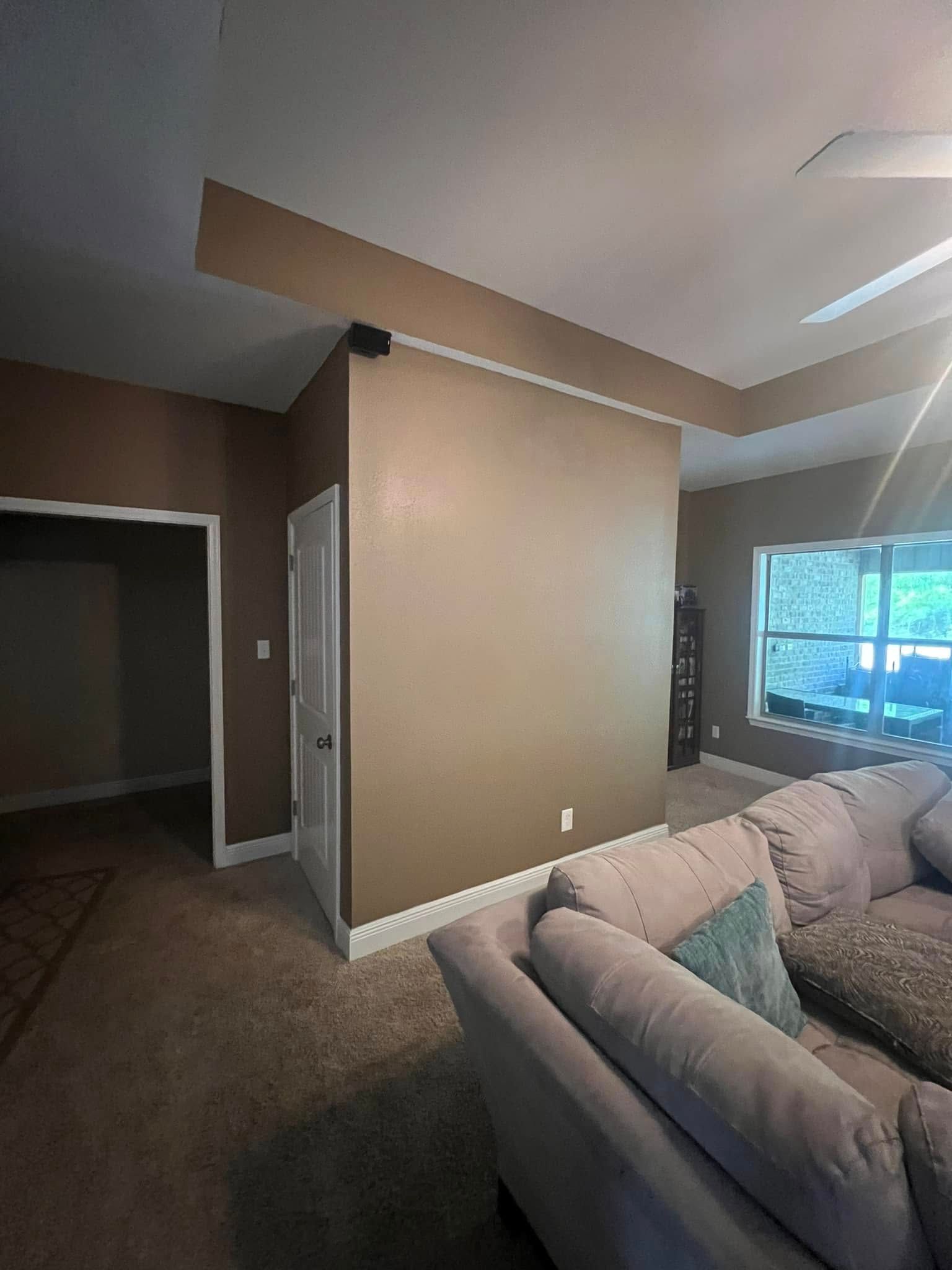 Interior view: A living room with brown walls, a sectional sofa, doorway to a hallway, and a window with natural light.