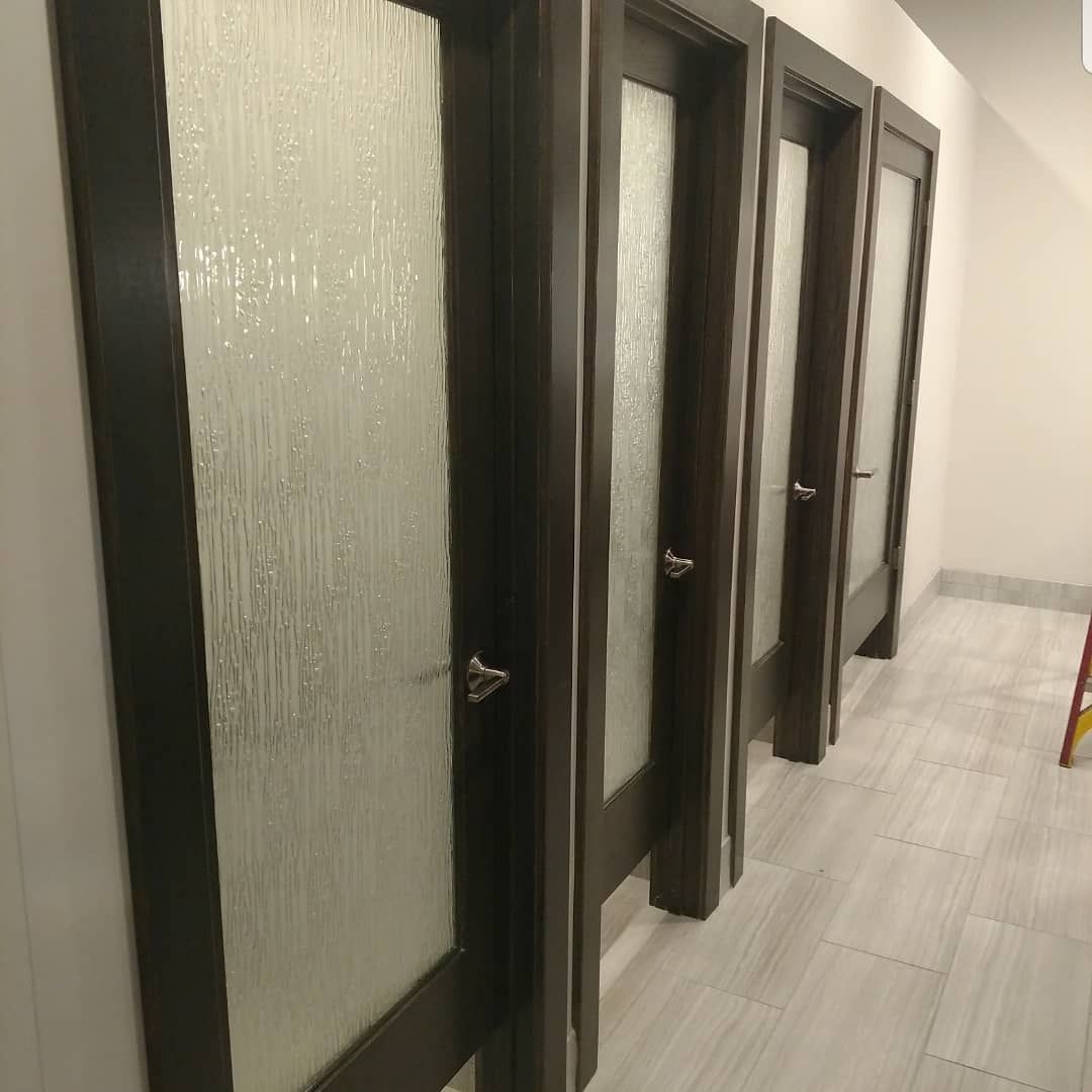 Four dark framed doors with textured glass panels line a hallway with light tile flooring and white walls.