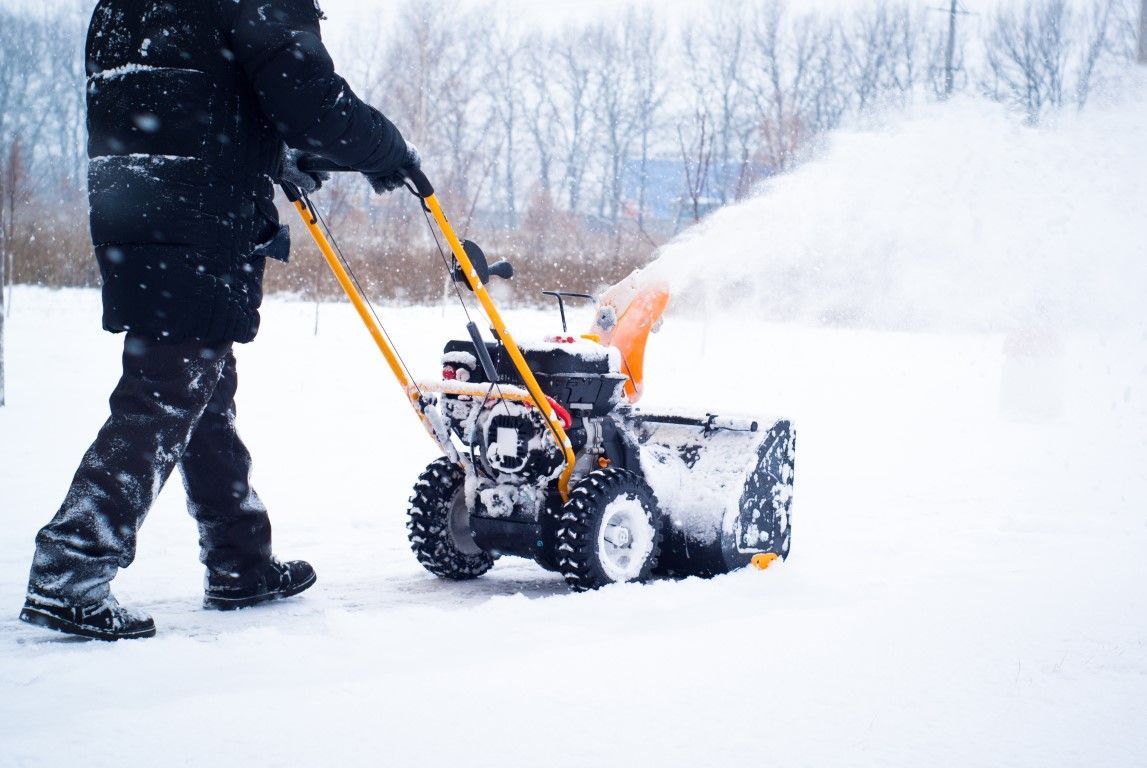Person clearing snow with a yellow snow blower in a snowy yard