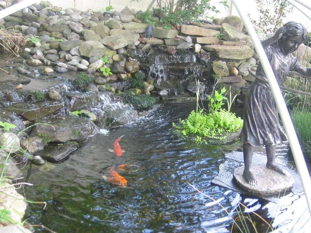 A statue of a woman standing in a pond with fish.